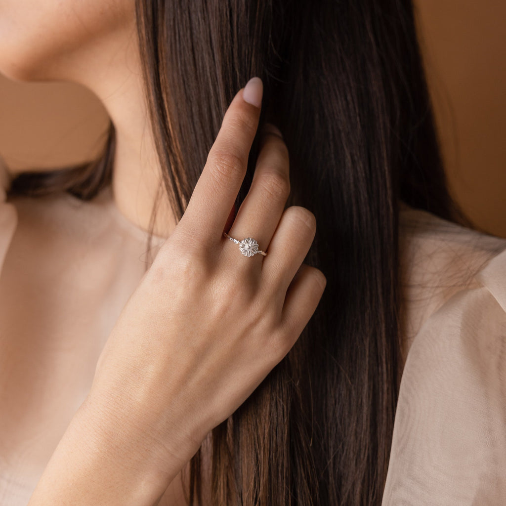 A woman touches her long brown hair, wearing the Flower Birthstone Ring—a sparkling, vintage-inspired accessory—on her left hand.