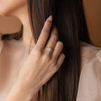 A woman touches her long brown hair, wearing the Flower Birthstone Ring—a sparkling, vintage-inspired accessory—on her left hand.