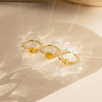 Three Flower Birthstone Rings with yellow and blue gemstones rest on a light, textured surface with soft shadows.