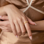 Close-up of a woman's hand wearing the Alicia Pearl Inlay Band, a gold stackable ring with pearl details, against a beige satin dress.