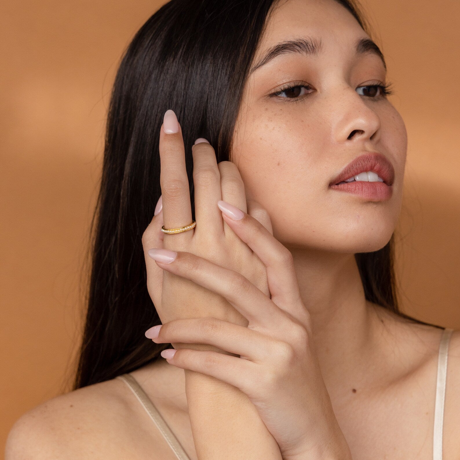 A woman with long dark hair displays manicured nails and the Alicia Pearl Inlay Band, posing against a warm beige background.