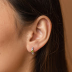Close-up of a woman's ear wearing Peridot Heart Huggies—a minimalistic earring with a small silver hoop and a vibrant green peridot heart gemstone.