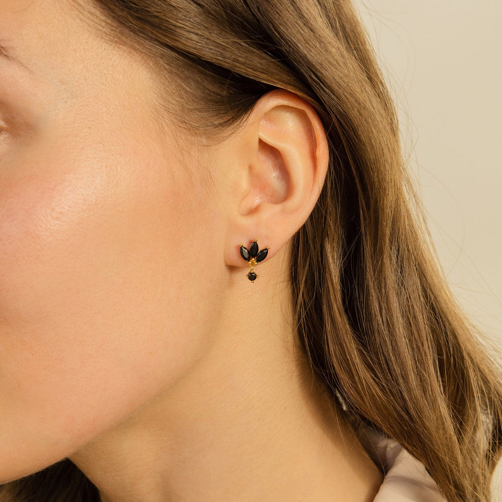 A close-up of a woman wearing Emily Drop Earrings—small, black and gold leaf-shaped studs on her left ear—ideal for fans of subtle statement jewelry.