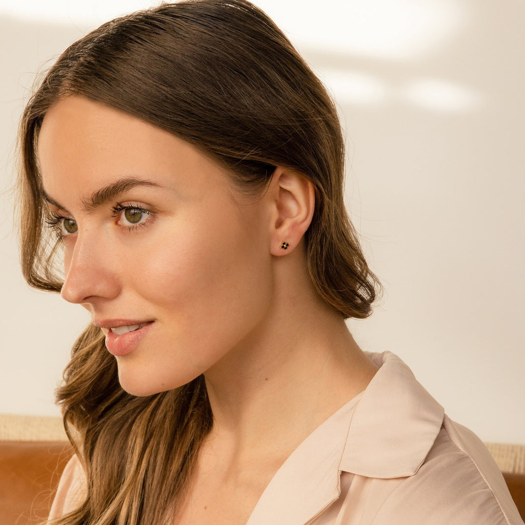Woman with long brown hair wearing Black Flower Studs, looking to the side in soft natural lighting.