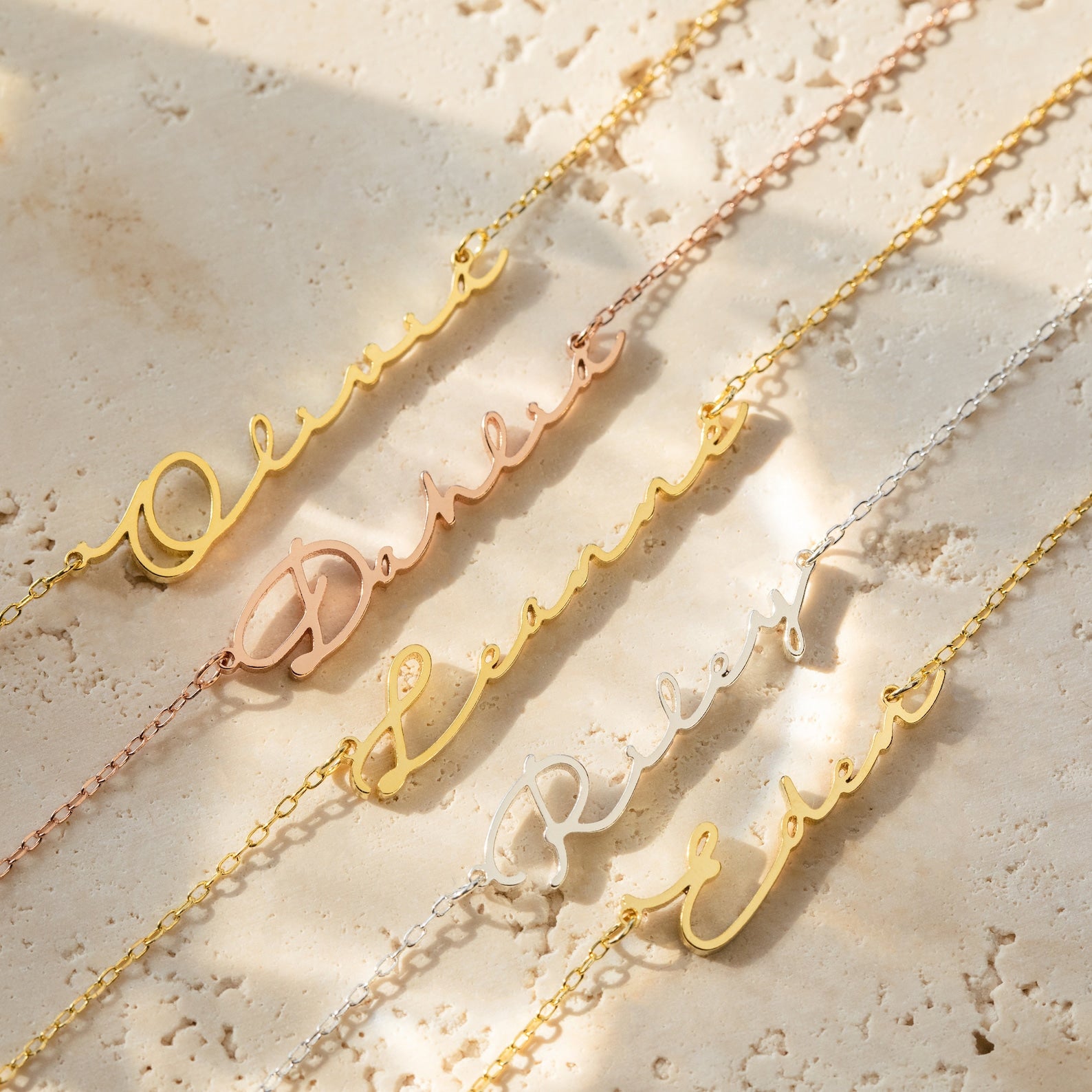 Four Minimal Sideways Name Necklaces in gold and silver, personalized with Olivia, Dakota, Riley, and Elena, rest on a beige stone surface—each dainty accessory features an elegant sideways design.