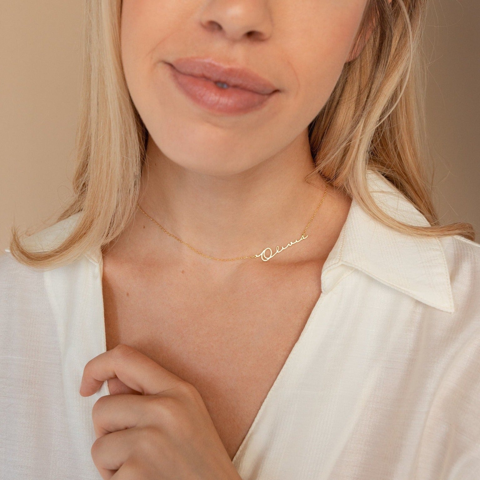 A woman wears a white shirt paired with the Minimal Sideways Name Necklace, a delicate gold piece featuring an off-center name pendant—perfect as a dainty accessory.