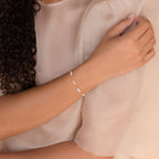 A woman wears a sheer, light blouse with the Hali Pearl Station Bracelet—an elegant accessory featuring delicate pearls and charms, perfect as a bridesmaid gift or refined bridal jewelry.