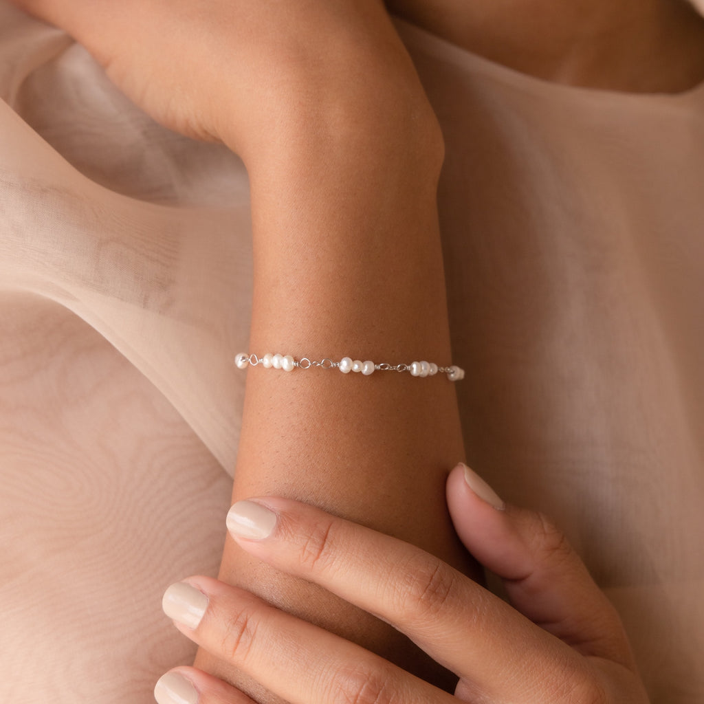 The Hali Pearl Station Bracelet graces a woman's wrist as her hand rests gently on her arm—an elegant accessory for brides or a thoughtful gift for bridesmaids.