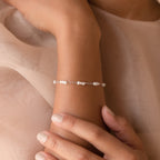 The Hali Pearl Station Bracelet graces a woman's wrist as her hand rests gently on her arm—an elegant accessory for brides or a thoughtful gift for bridesmaids.