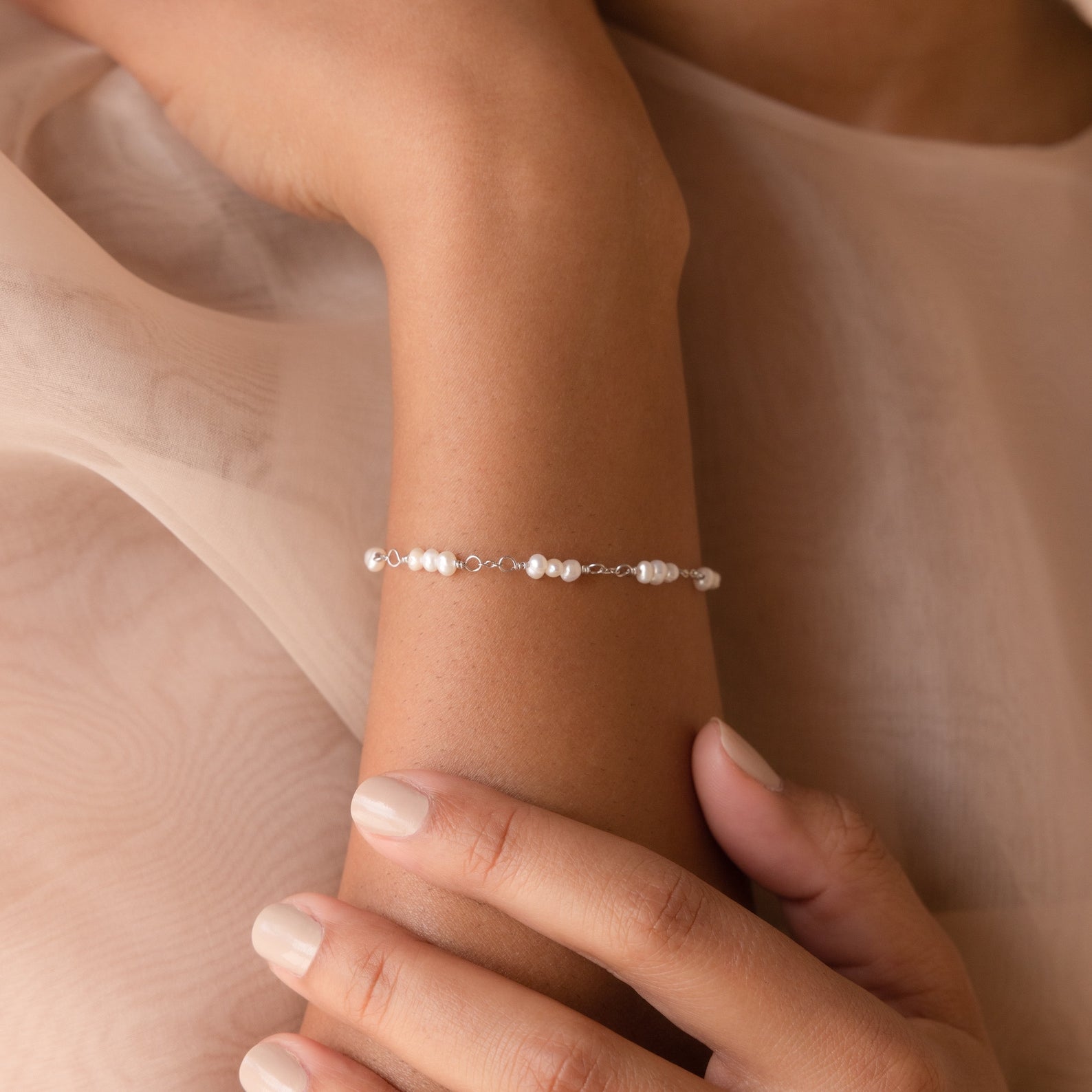 The Hali Pearl Station Bracelet graces a woman's wrist as her hand rests gently on her arm—an elegant accessory for brides or a thoughtful gift for bridesmaids.