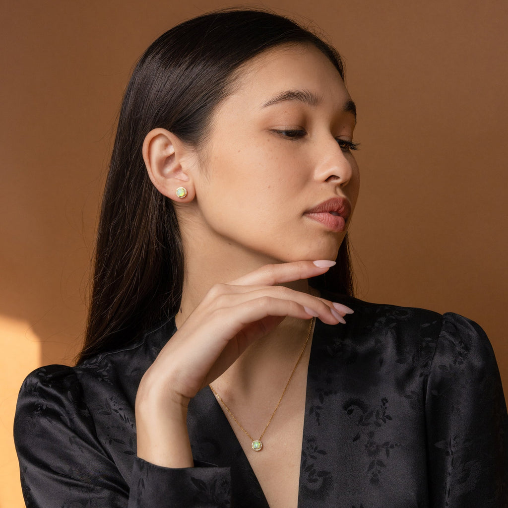 Woman in black blouse wears matching green earrings and a bold Halo Birthstone Necklace, posing against a brown background.