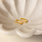 The Rayne Pearl Link Earrings, featuring gold hoops with small freshwater pearls, rest in a white scalloped ceramic dish—an elegant minimalist jewelry accent.