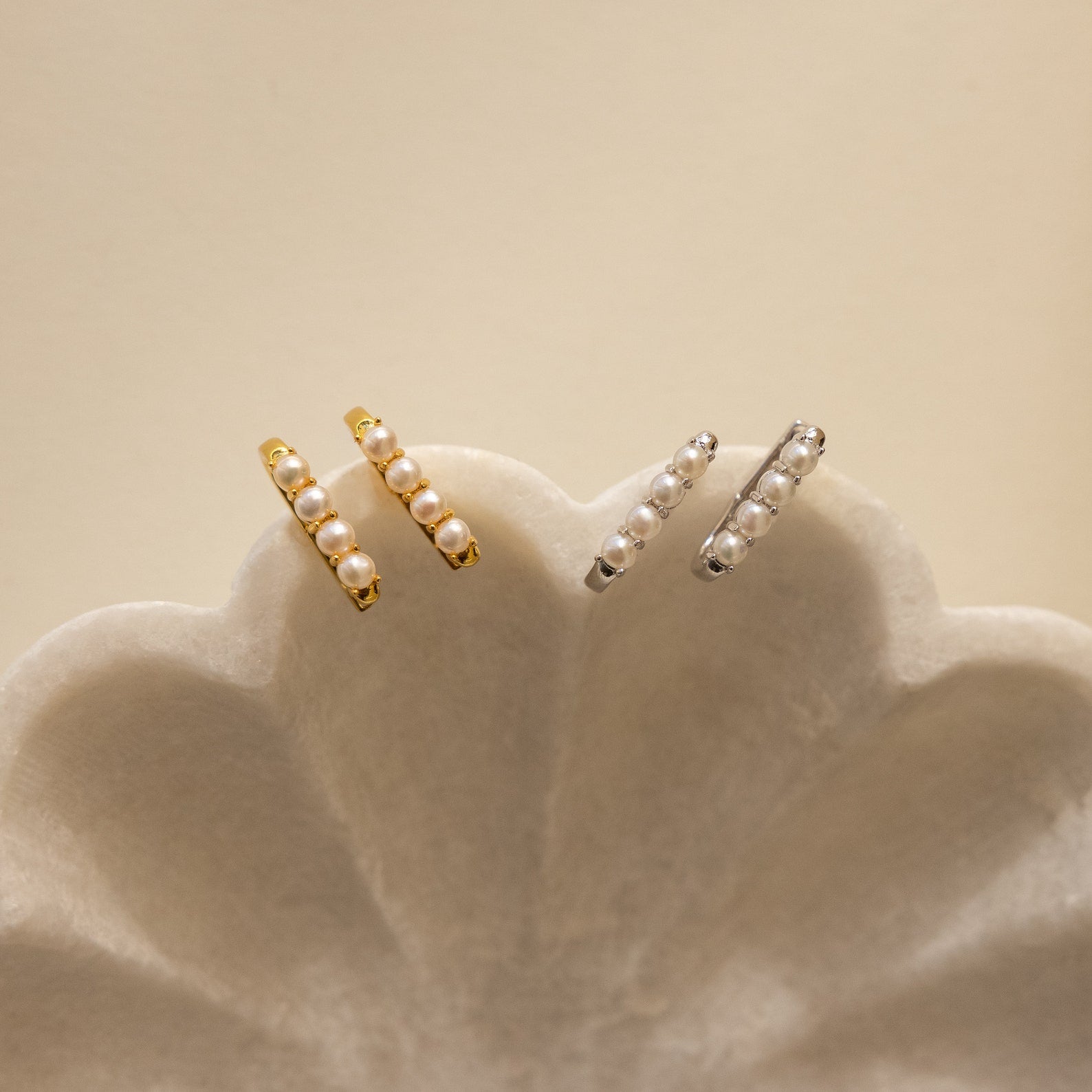 The Rayne Pearl Link Earrings, featuring gold and silver hoops with three freshwater pearls each, are displayed on a scallop-shaped white dish—ideal for fans of minimalist jewelry.