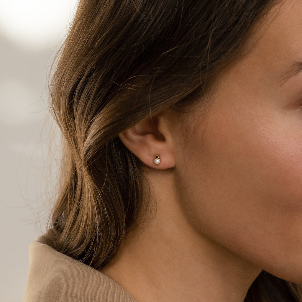 A close-up of a woman's ear adorned with elegant Raindrop Pearl Onyx Studs.