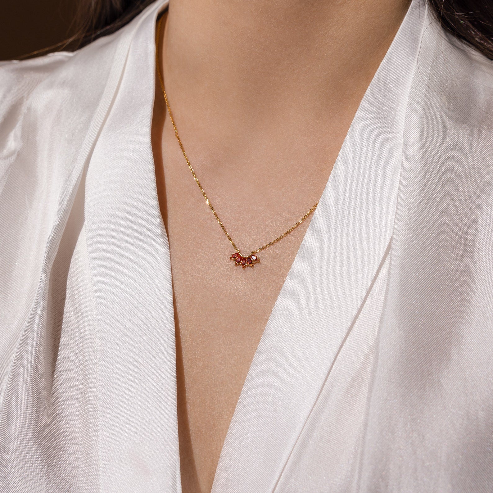 A person wearing a white satin blouse and the Marquise Birthstone Necklace featuring a small red pendant.
