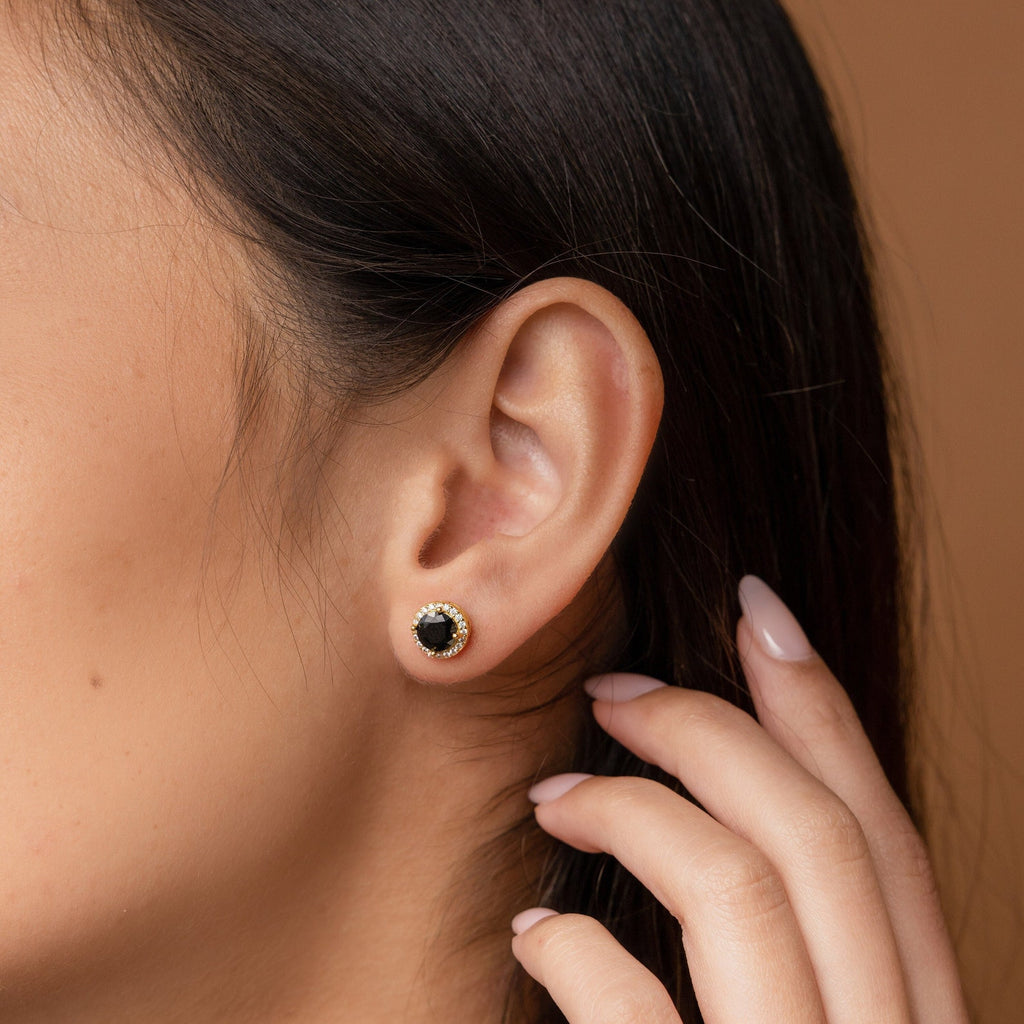Close-up of a woman's ear wearing Halo Birthstone Studs, with her hand touching her hair against a neutral background.