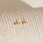 Triple Birthstone Studs featuring gold and small pearls, reminiscent of elegant birthstone earrings, displayed on a textured, cream-colored surface.