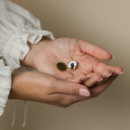 A person holding the Pearl Disc Locket Necklace with an open locket displaying a silhouette portrait, wearing a white ruffled sleeve—a meaningful gift to cherish treasured memories.