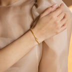A woman's hand wears the Large Letter Bracelet, featuring a gold curb chain with a personalized A charm, resting on sheer beige fabric—an ideal choice for everyday jewelry.