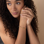 A woman with curly hair wears the Rainbow Station Bracelet, resting her chin on her hands and looking thoughtful.
