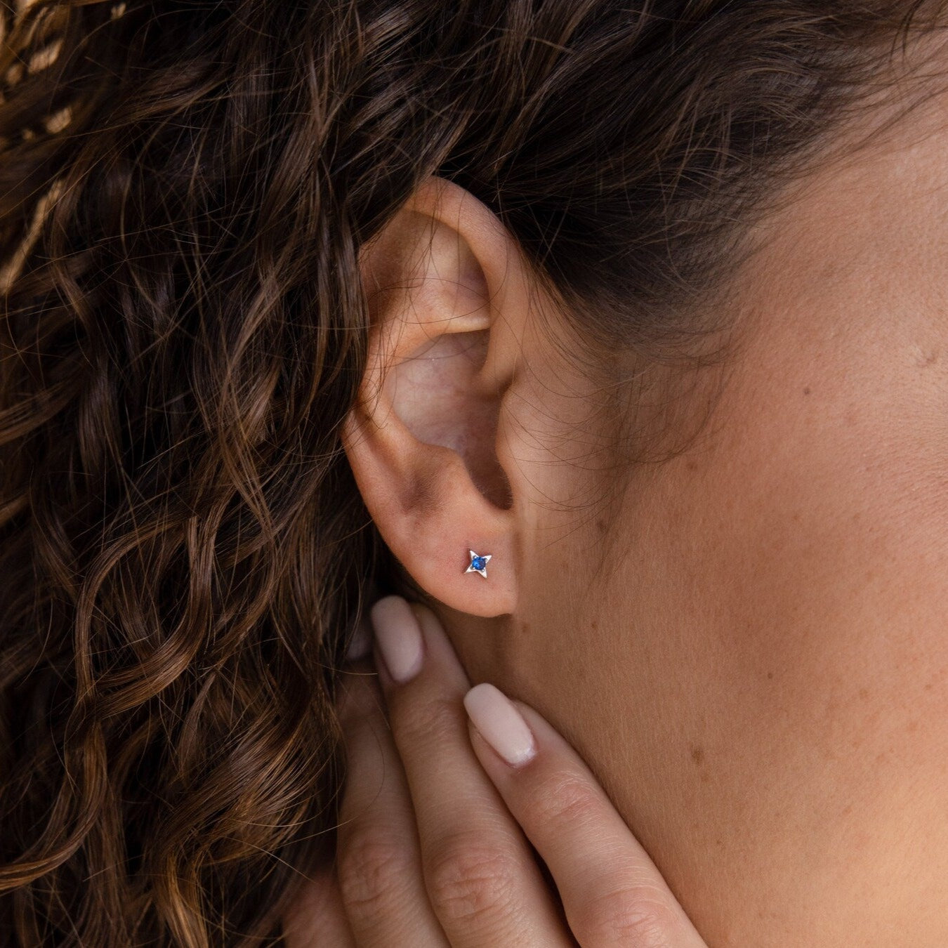 Close-up of a woman’s ear adorned with Sapphire Star Studs; her hand gently touches her neck, drawing attention to an elegant cartilage piercing.