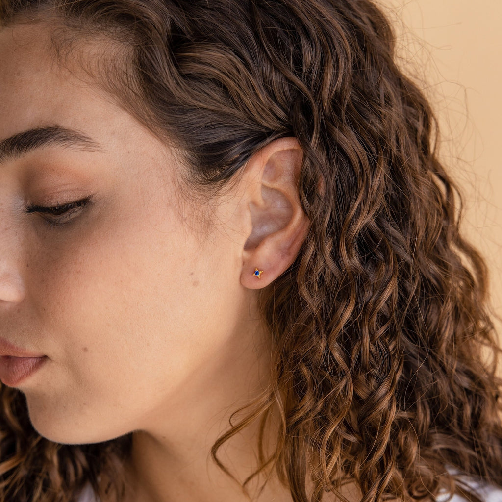 Woman with curly hair wearing Sapphire Star Studs, celestial star-shaped earrings ideal for cartilage piercings, shown in close-up profile.