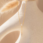 The Leena Diamond Lariat Necklace, featuring a delicate chain and two sparkling diamond pendants, is displayed on a smooth, cream-colored sculptural surface.