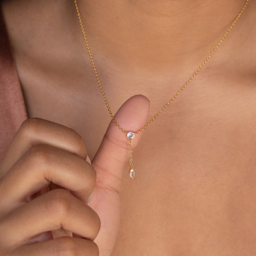 A hand holds the Leena Diamond Lariat Necklace, showcasing its delicate chain and two small diamond pendants in a subtle dangle design against bare skin.