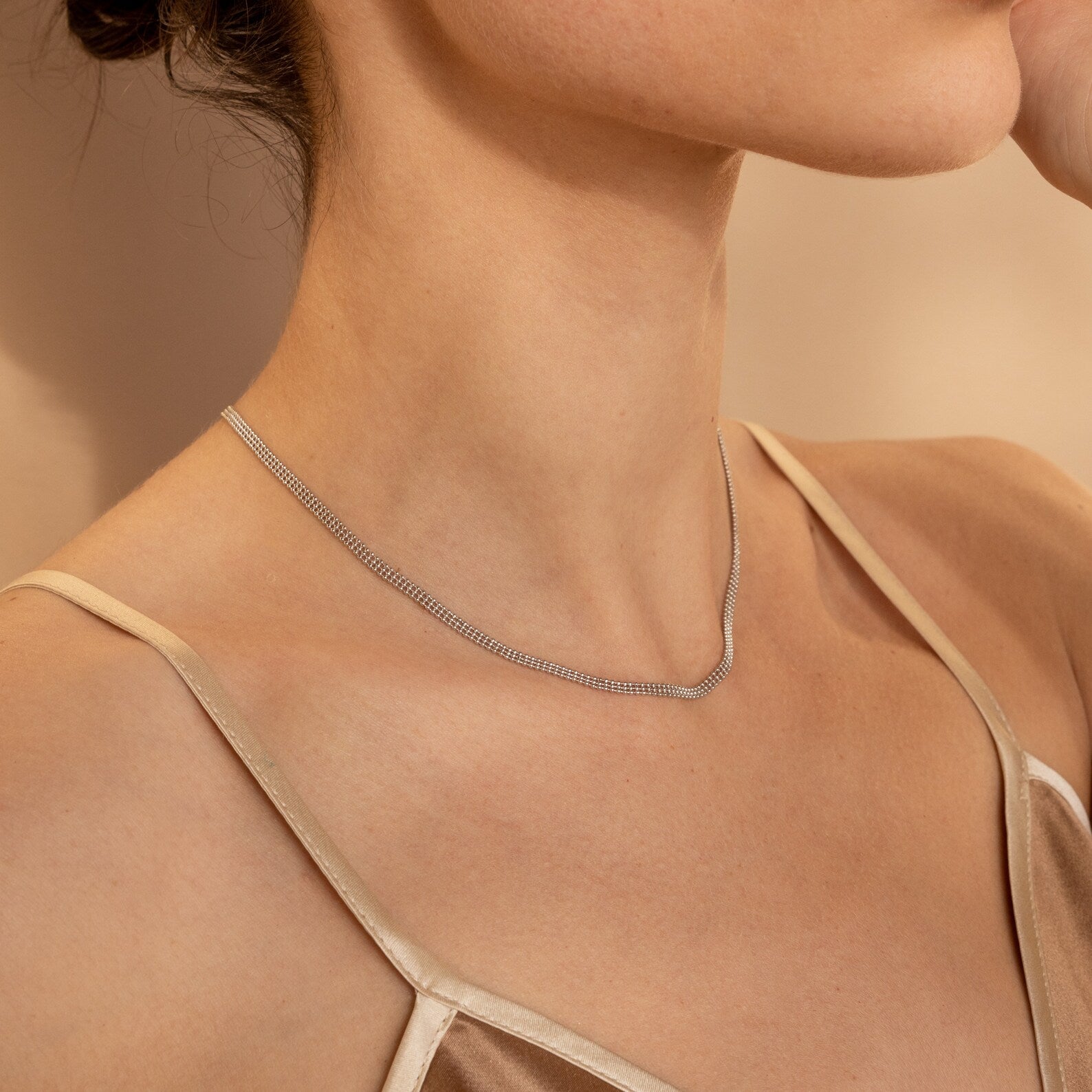 A woman wearing the Tri-Stacked Beaded Necklace and a beige spaghetti strap top against a neutral background.
