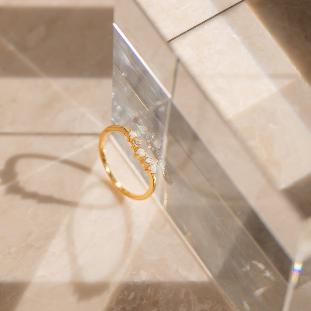 The Layla Opal Diamond Ring, adorned with delicate stones, rests on a reflective surface and casts a shadow across beige tiles.