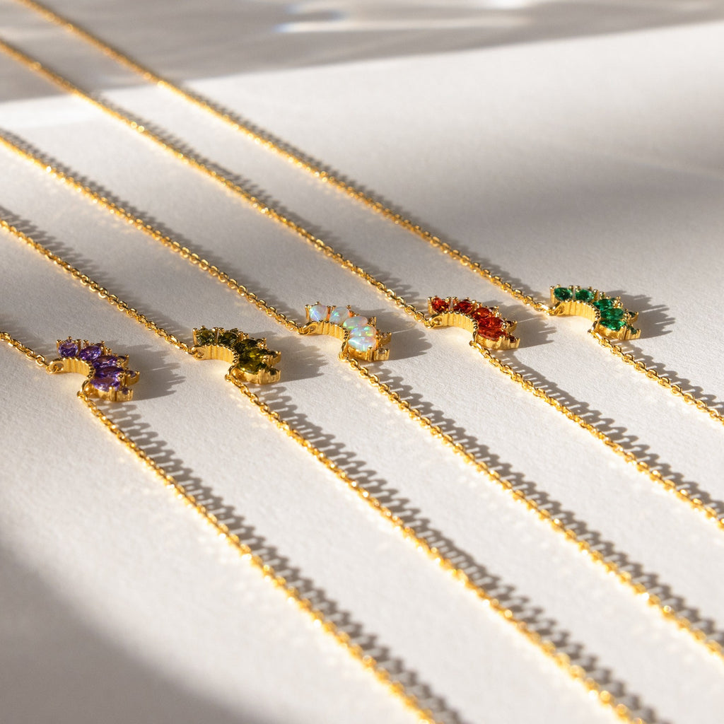 Five Marquise Birthstone Necklaces with colorful gemstone pendants are arranged in a neat row on a white surface.