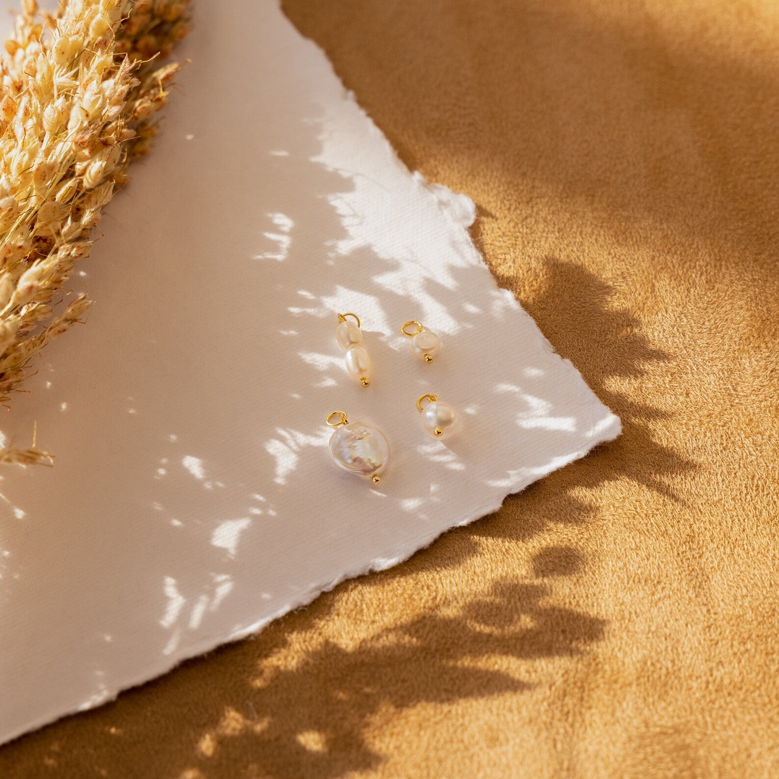 The Pearl Drop Earrings Set is displayed on white textured paper with dried flowers and a brown fabric background—ideal minimalist earrings for bridal elegance.