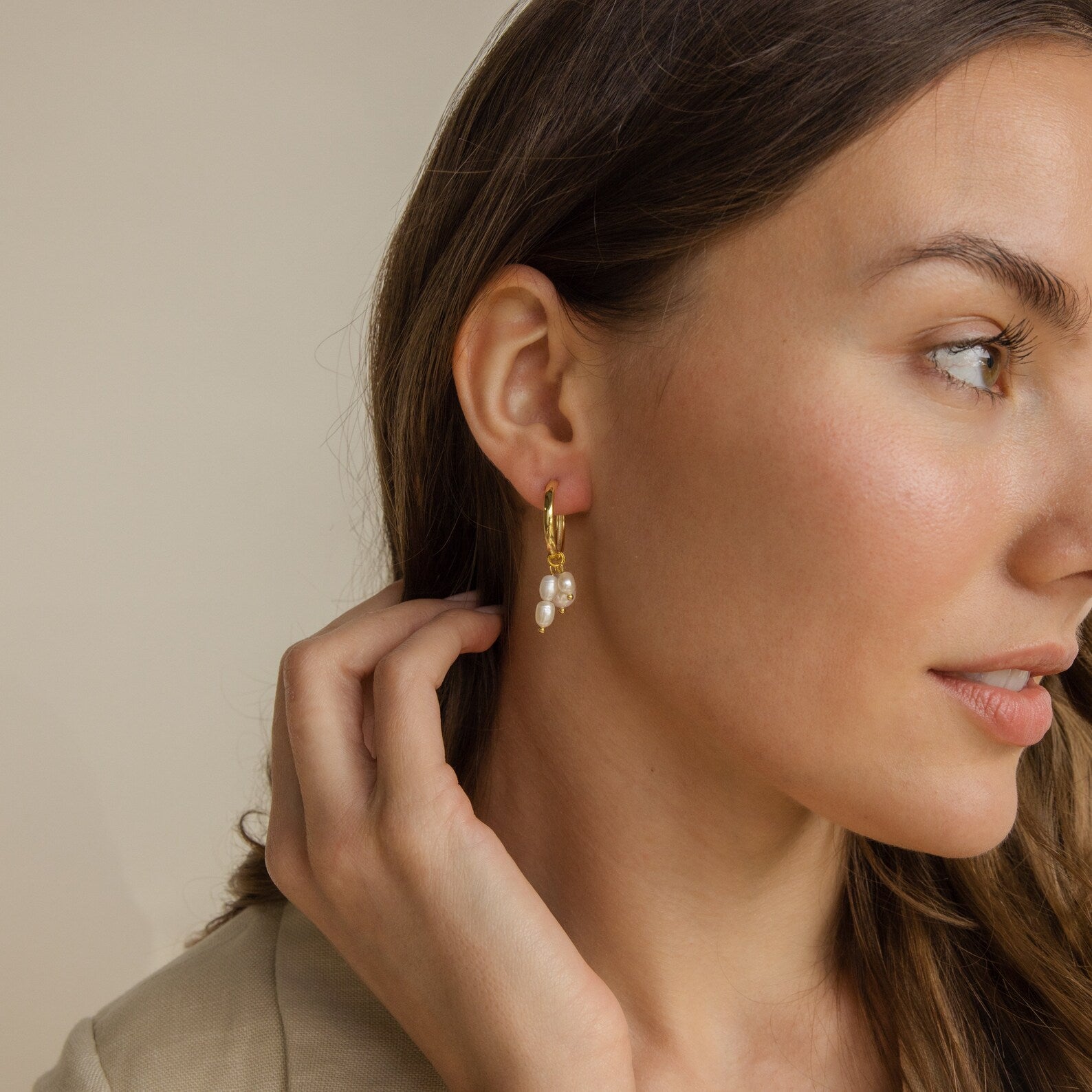 A woman touches her hair while wearing the Pearl Drop Earrings Set—featuring minimalist gold hoops and pearls—an elegant choice for bridal earrings.