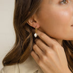 A woman touches her gold Pearl Drop Earrings Set, featuring a dangling white pearl—an elegant, minimalist or bridal choice. The close-up highlights her face, hand, and the earrings' graceful detail.