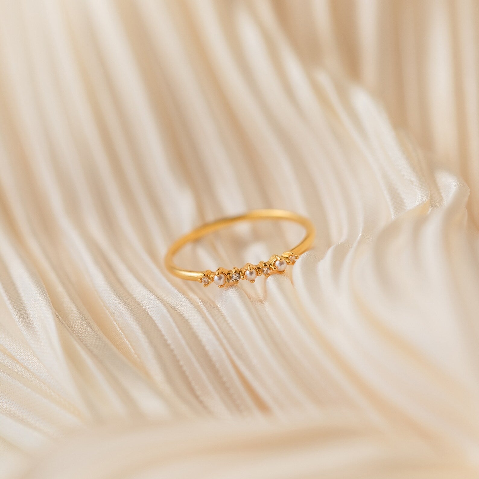 The Delicate Pearl Diamond Ring, adorned with small diamonds, is displayed on soft, cream-colored fabric with gentle folds.