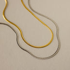 Gold and silver herringbone chain necklaces with a sleek, flat design, displayed side by side on a neutral background.