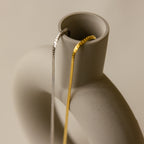 A Thick Snake Chain Necklace in gold draped over the rim of a matte, modern ceramic vase.