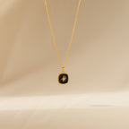 Hermoine Pendant Necklace with a gold chain and black pendant accented by a small star design, shown on a beige background.