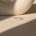 The Crescent Opal Ring rests on a beige surface in gentle sunlight, with a curved ceramic object in the background.