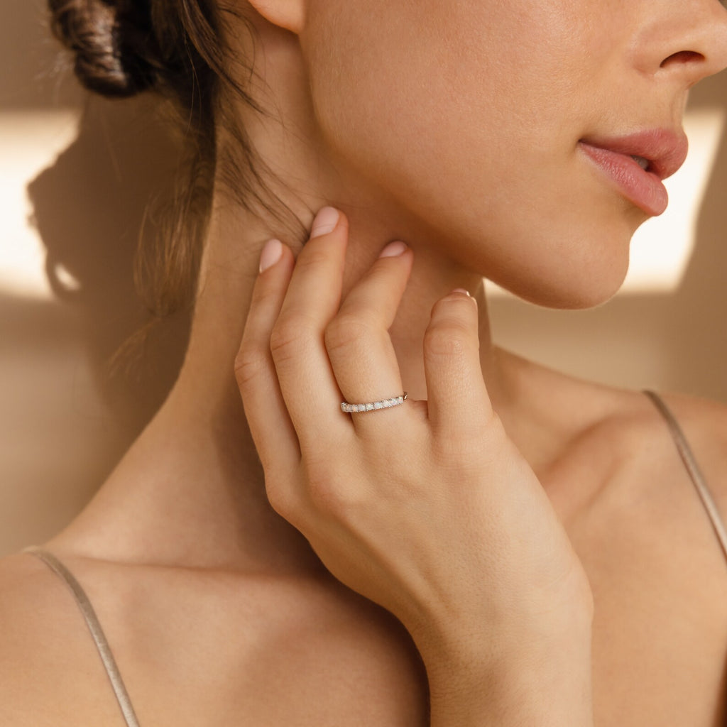 A woman gently touches her neck, showcasing the Crescent Opal Ring on her finger against a soft, neutral background.