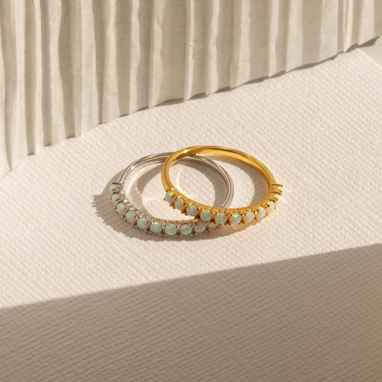 The Crescent Opal Ring, available in silver and gold, features stunning gemstones and is displayed on a textured cream surface with soft shadows—perfect as an anniversary gift or an elegant promise ring.