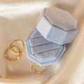 The 3 Slot Velvet Ring Box in light blue is open beside three gold rings on cream-colored fabric, creating an elegant jewelry display.