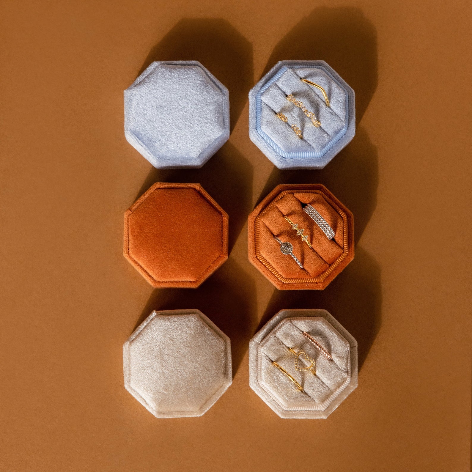 The Mystery Ring Box comes in blue, orange, and beige velvet octagons—some open to display gold jewelry inside—making each box a charming addition to your collection.