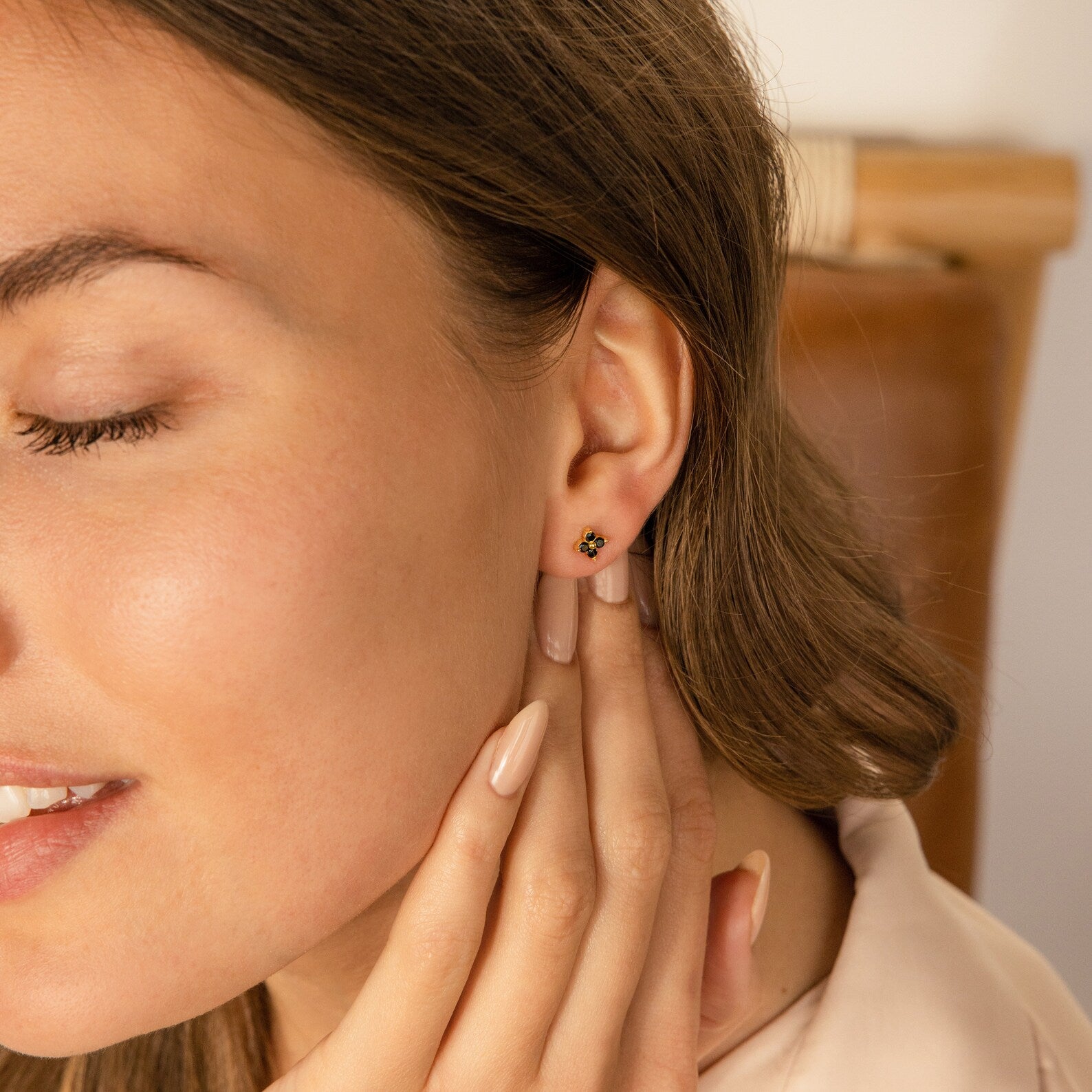 Woman with closed eyes touches her neck, wearing Black Flower Studs styled like vintage earrings and subtle nude nail polish.