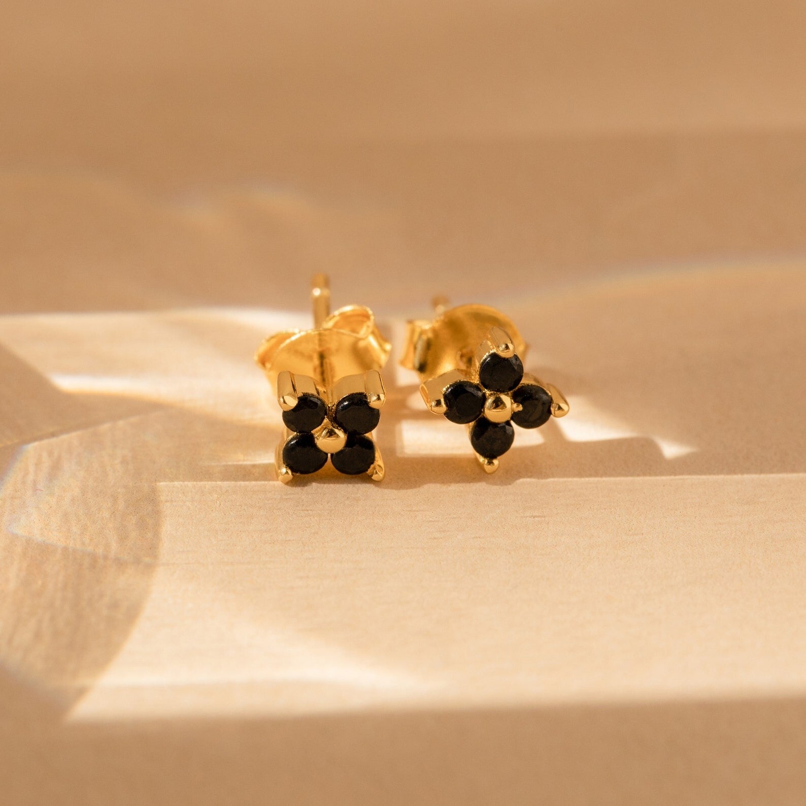 Black Flower Studs: Gold Art Deco earrings featuring a black stone flower design, shown on a beige surface in soft sunlight.