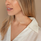 Woman wearing a cream blouse and gold Minimal Sideways Name Necklace, shown from the shoulders up—a delicate, dainty accessory that complements any outfit.