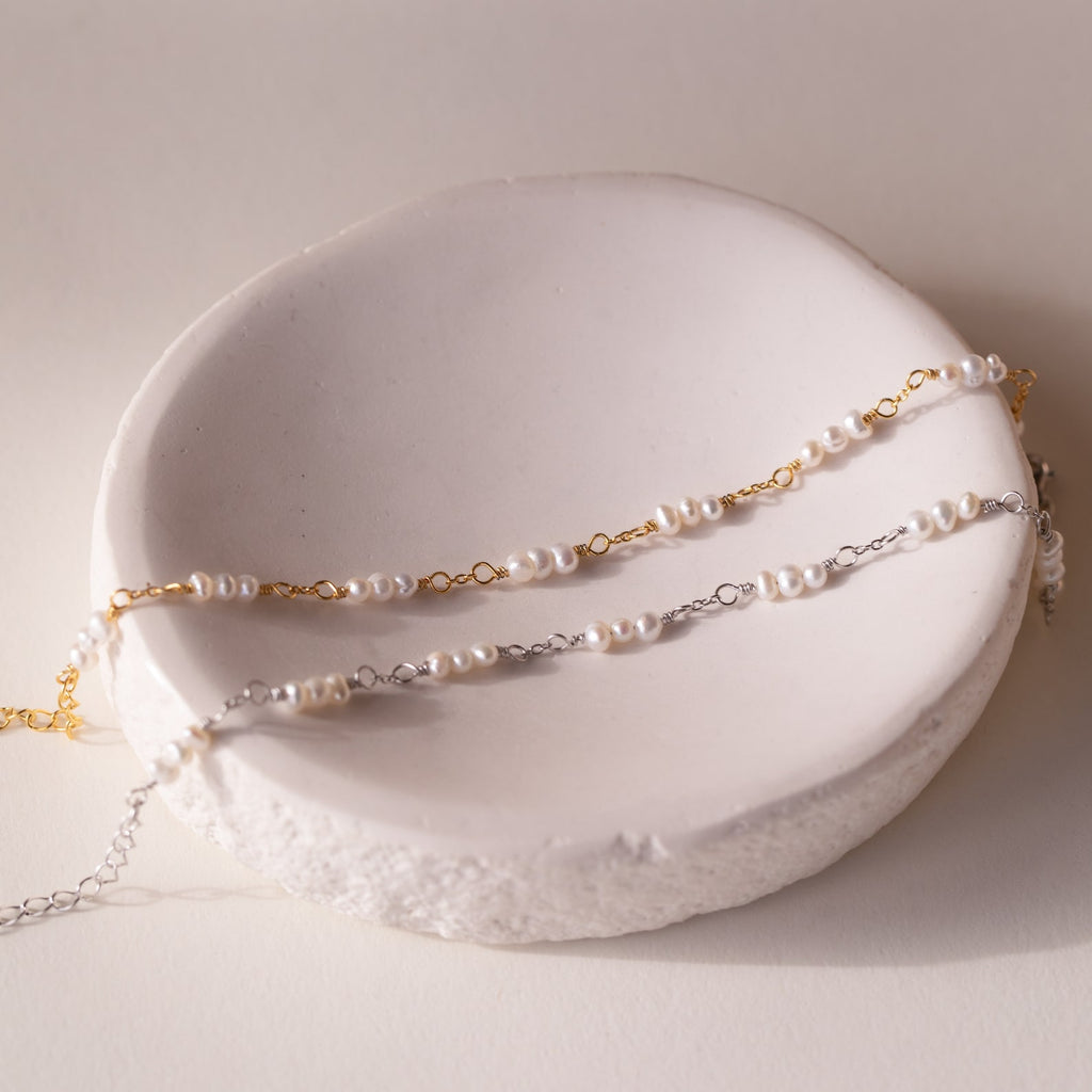 The Hali Pearl Station Bracelet features a delicate pearl chain in your choice of gold or silver—beautifully displayed on a white ceramic dish, it's an ideal bridesmaid gift or timeless piece of bridal jewelry.