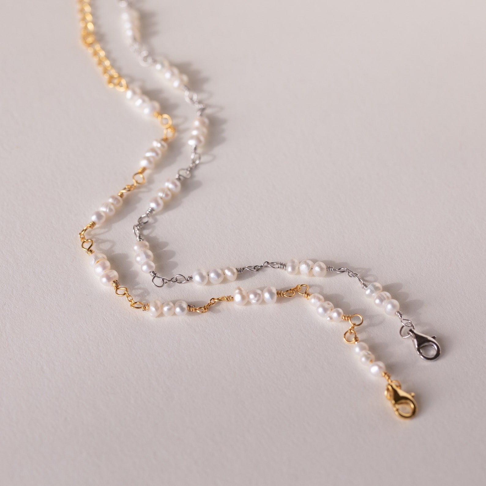 The Hali Pearl Station Bracelet with gold and silver clasps is displayed on a light surface—an elegant choice for bridal jewelry or a thoughtful bridesmaid gift.