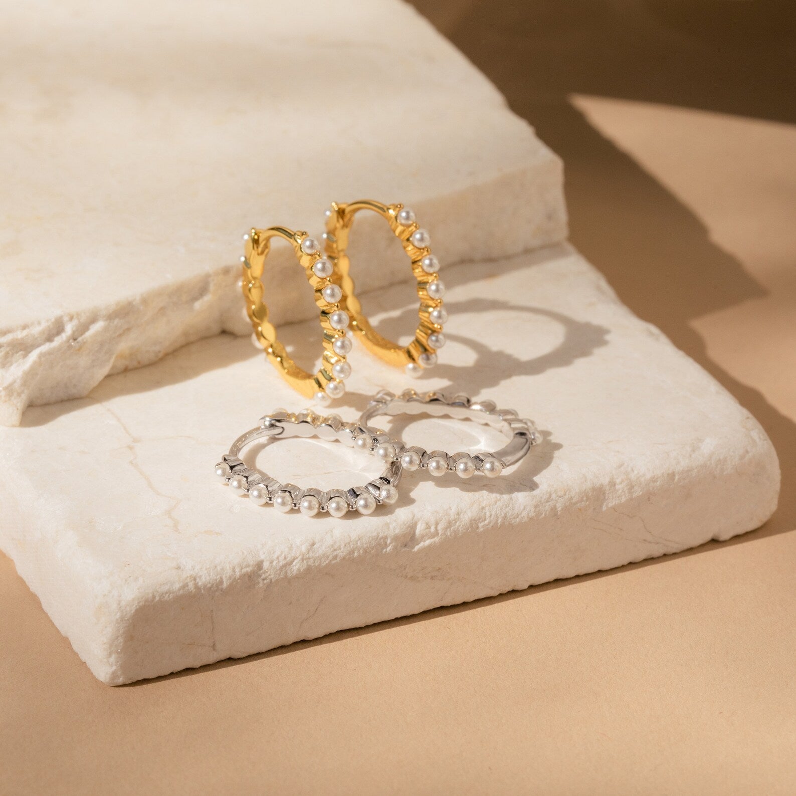 Malik Pearl Hoops—gold and silver pearl earrings with delicate accents—make stunning minimalist or wedding jewelry, beautifully displayed on white stone slabs in gentle lighting.