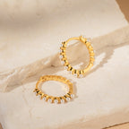 The Malik Pearl Hoops feature a minimalist design with small pearls, displayed on light-colored stone slabs—ideal as elegant wedding jewelry or for everyday wear.